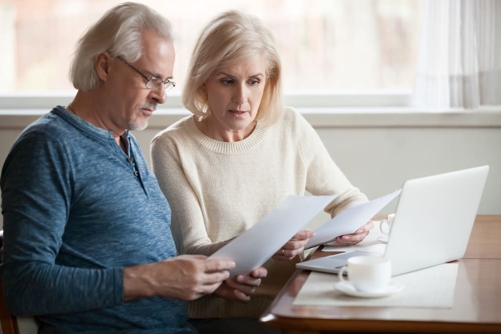 Retired couple looking at paperwork and sitting in front of a laptop.